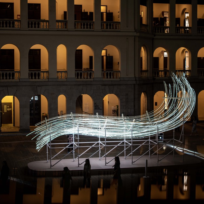 Modern art installation with wavy light tubes in a courtyard.
