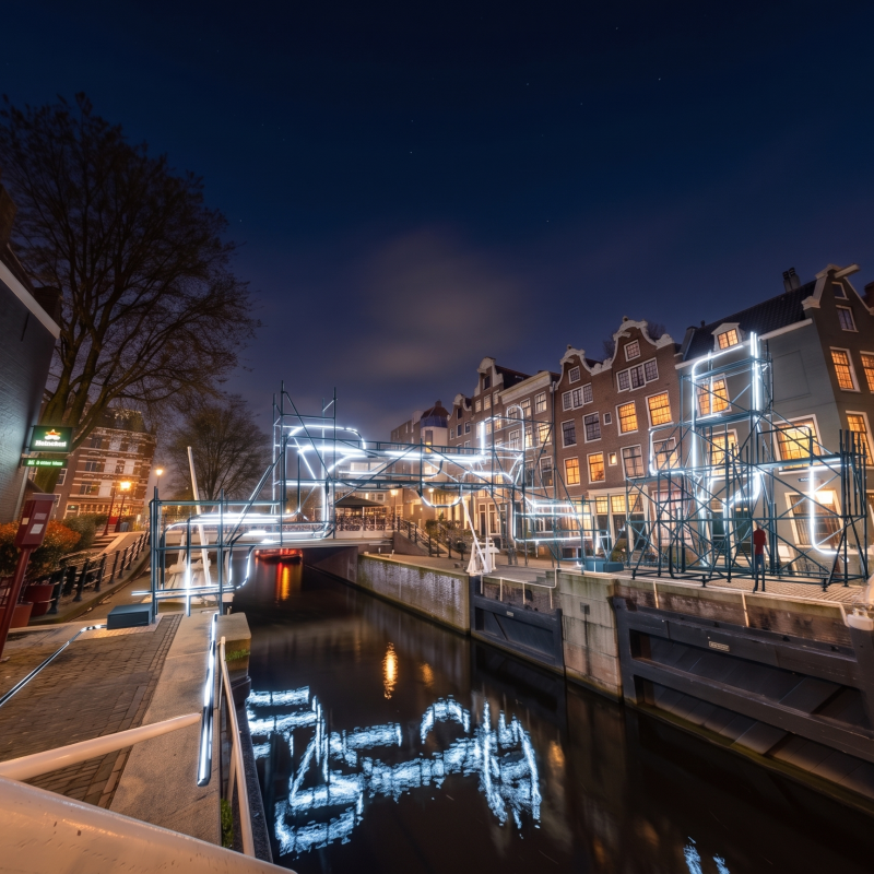 Night scene of a canal with illuminated decorations and historic buildings.
