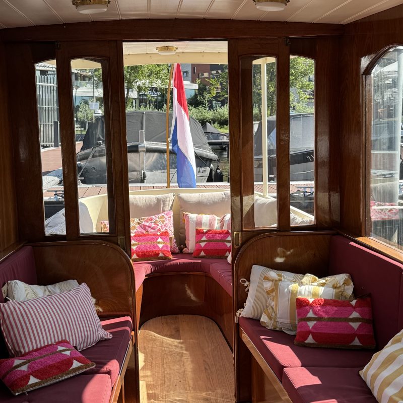 Interior of a small boat with colorful cushions and a flag outside the window.