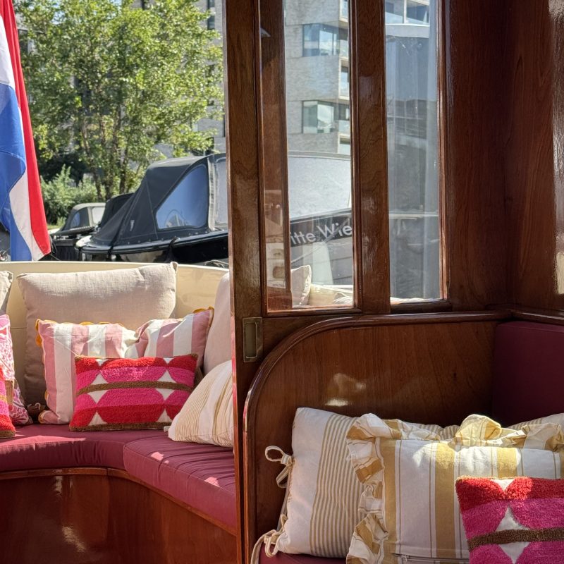 Boat interior with pink cushions, colorful pillows, and a flag in the background.