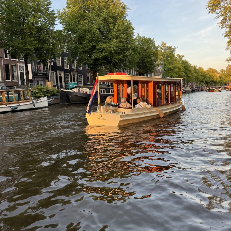 A boat with passengers cruising on a tree-lined canal during sunset.