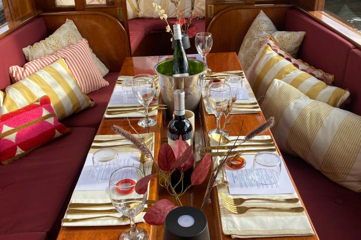 Elegant boat dining setup with wine, glasses, cushions, and decorative leaves.
