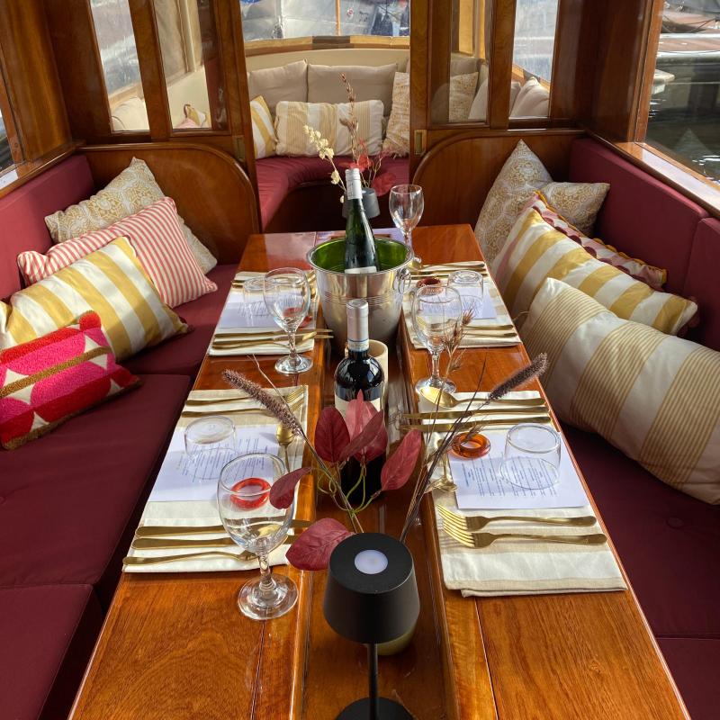 Elegant boat dining setup with wine, glasses, cushions, and decorative leaves.