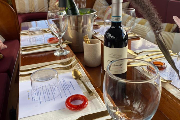 Elegant dining setup on a boat with wine bottles, glasses, and golden cutlery on a wooden table onboard Leaudine