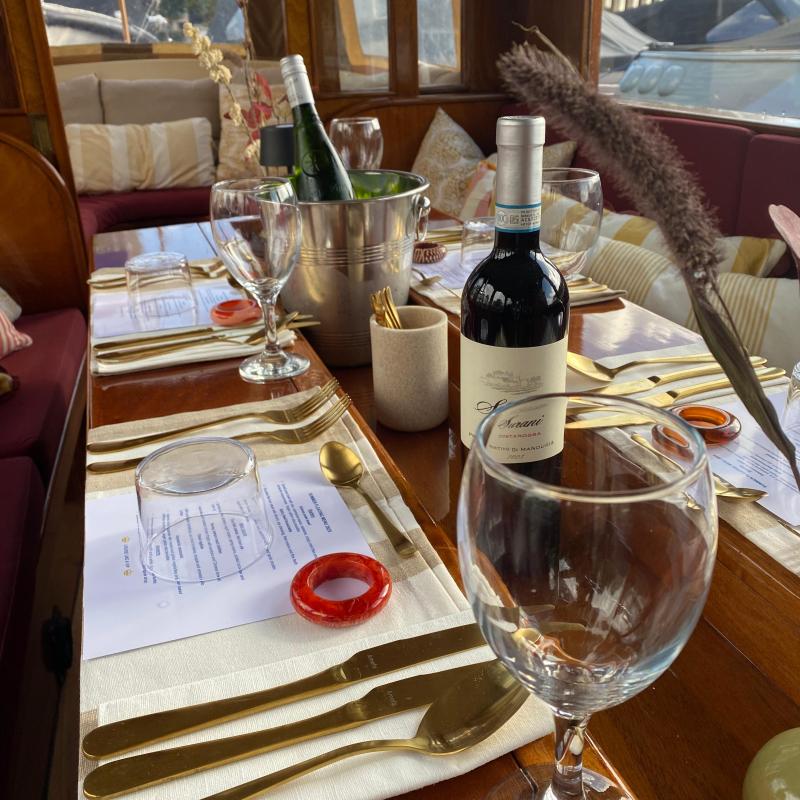 Elegant dining setup on a boat with wine bottles, glasses, and golden cutlery on a wooden table onboard Leaudine
