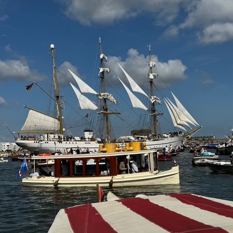 Sailing ship and boats on blue water under a partly cloudy sky.